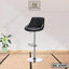 Modern black leather bar stool with chrome base and footrest in a minimal indoor setting