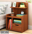 Wooden bedside table with shelves, a drawer, books, decor items, and a clock beside a bed.