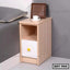 Modern wooden bedside table with storage drawer and open shelf, next to a bed.