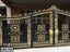Decorative black and gold metal boundary gate with ornate floral patterns, outdoor setting