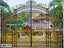Ornate golden black wrought iron boundary gate with intricate designs in front of a house