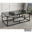 Modern black metal and glass center table with geometric frame, books, and decorative lamp.