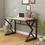 Modern computer table with black metal frame, laptop, books, and decorative plants in a home office.
