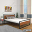 Modern double steel bed with wood accents in a bright bedroom, two pillows, side table, indoor plant, large window curtains.