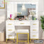 Modern white dressing table with mirror lights, makeup organizer, and cushioned stool in bedroom.