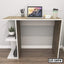 Modern office desk with laptop, coffee cup, books, and plant on wooden floor
