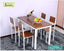 Wooden dining table set with four chairs, fruit bowl, and wine bottle on a gray rug