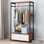 Standing closet organizer with hanging clothes, shelves, and storage drawer in a bedroom.