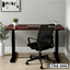 Standing computer desk with dark wood top, black frame, office chair, and potted plant