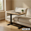 Modern standing desk with wooden top and black base beside a beige sofa in a bright room