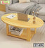 Modern oval wooden tea table with storage shelf, laptop, and vase in a living room setting.