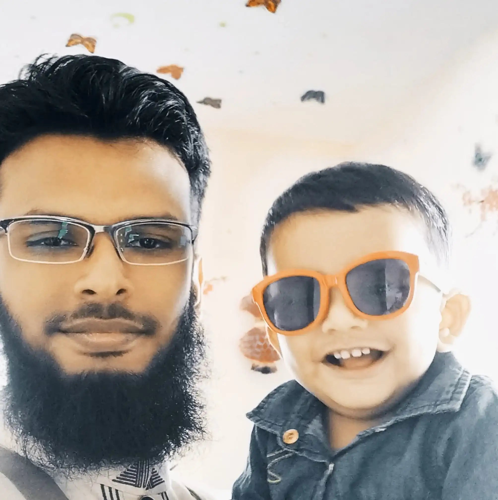 Man with beard and glasses and smiling child in sunglasses posing indoors