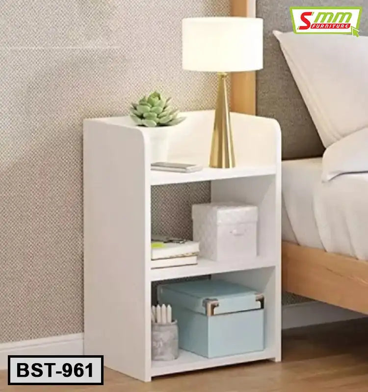 Modern white bedside table with shelves, lamp, decor, and storage boxes beside a bed