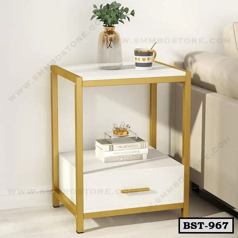 Modern gold and white bedside table with drawer, books, plant, and cup beside a sofa