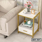 Modern bedside table with gold frame, white drawer, flowers, and decor beside a sofa