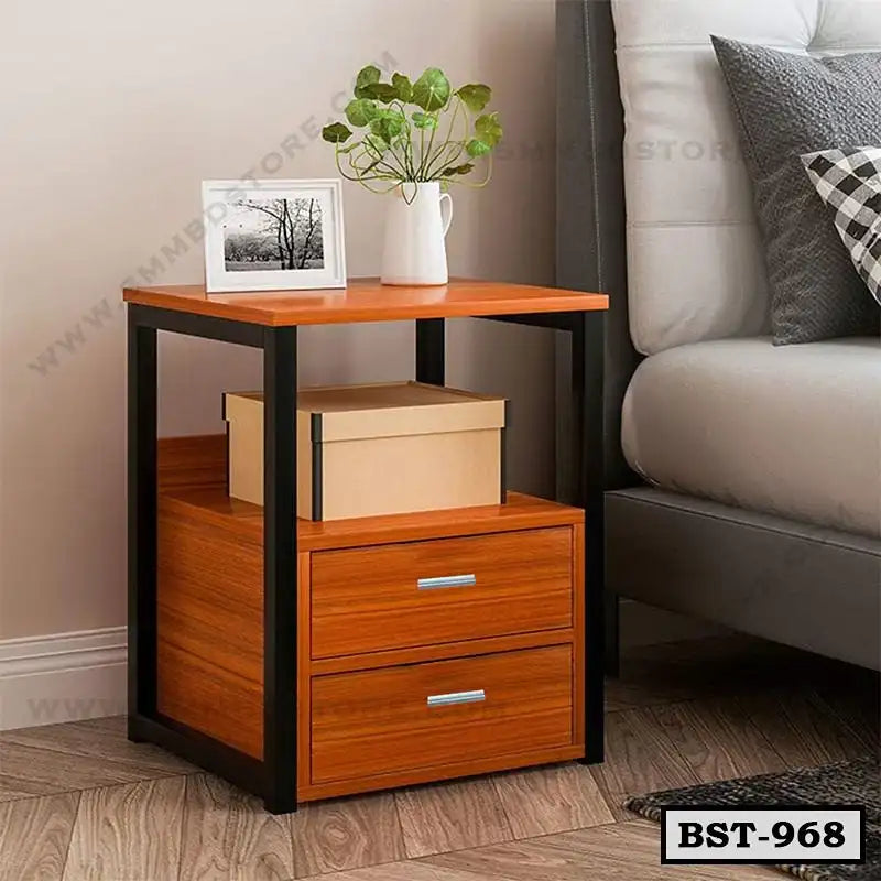 Modern wooden bedside table with black frame, two drawers, and decor items beside a bed Main image