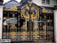 Ornate black and gold metal boundary gate with intricate decorative patterns in front of a house