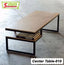 Modern wooden center table with black metal frame and lower shelf holding books on a concrete floor.