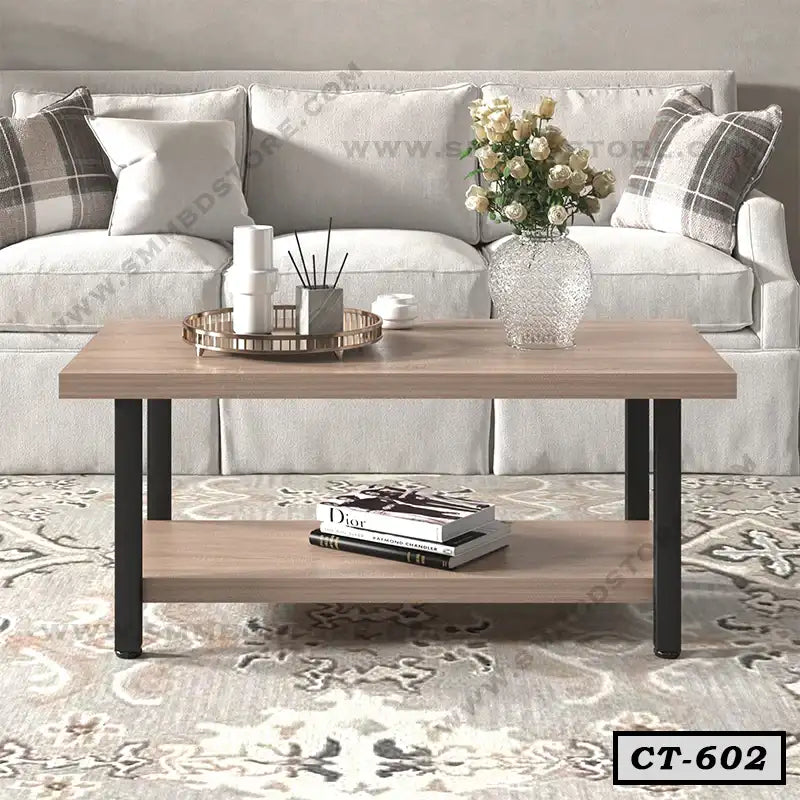 Modern wooden center table with black legs, vase, and tray, in front of a sofa in living room