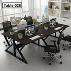 Modern four-person office desk with computers, mesh chairs, and indoor plants in workspace