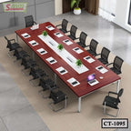 Large modern conference table with chairs, laptops, papers, and green plants in office setting