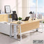 Modern executive office table with light wood finish, metal legs, and black mesh chair in bright room