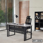 Modern executive office table with black steel frame and mesh chair, bookshelf in background