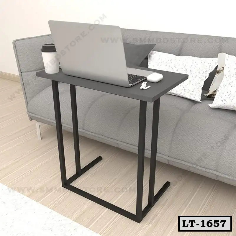 Modern black laptop table near a grey sofa and pillows in a home office setting