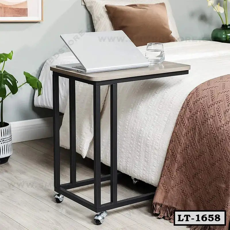Modern laptop table with wheels beside a bed, featuring a laptop and glass of water. Main image