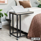 Modern laptop table with wheels beside a bed, featuring a laptop and glass of water.