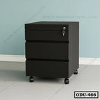 Black office drawer unit with three drawers and a lock, on wheels, against a blue wall