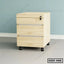 Light wood office drawer unit with lock and wheels on tiled floor against blue wall