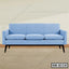 Modern light blue office sofa with three seat cushions and black legs on a wooden floor.