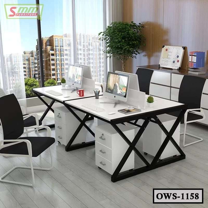 Modern office workstation desk with computers, black chairs, and storage drawers in a bright workspace