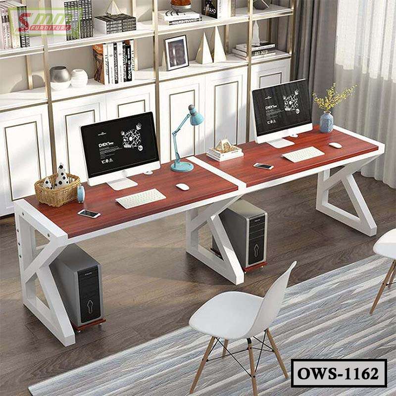 Modern dual office workstation desk with computers, chairs, and bookshelves in a bright office
