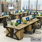 Modern office workstation setup with multiple desks, computers, office chairs, and indoor plants.