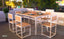 Modern wooden dining table set with six chairs on a balcony, set for dinner, with city view.