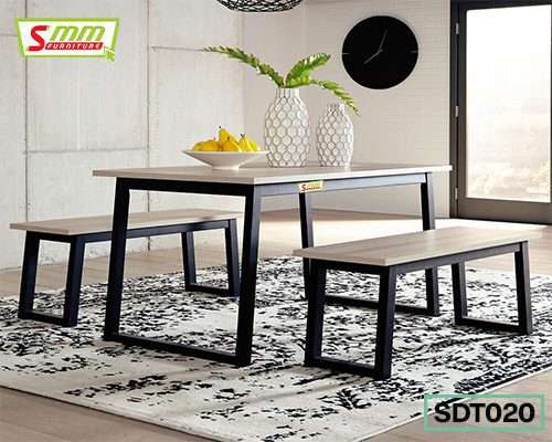 Modern dining table set with two benches, metal frames, on patterned rug in bright room
