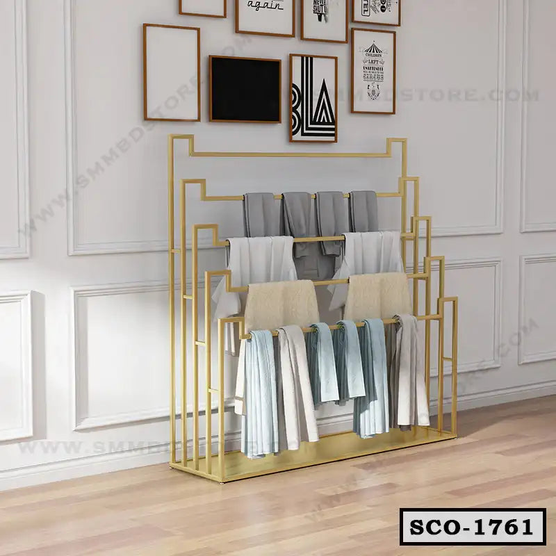 Modern gold metal standing closet organizer with multiple shelves holding folded clothes in a bright room