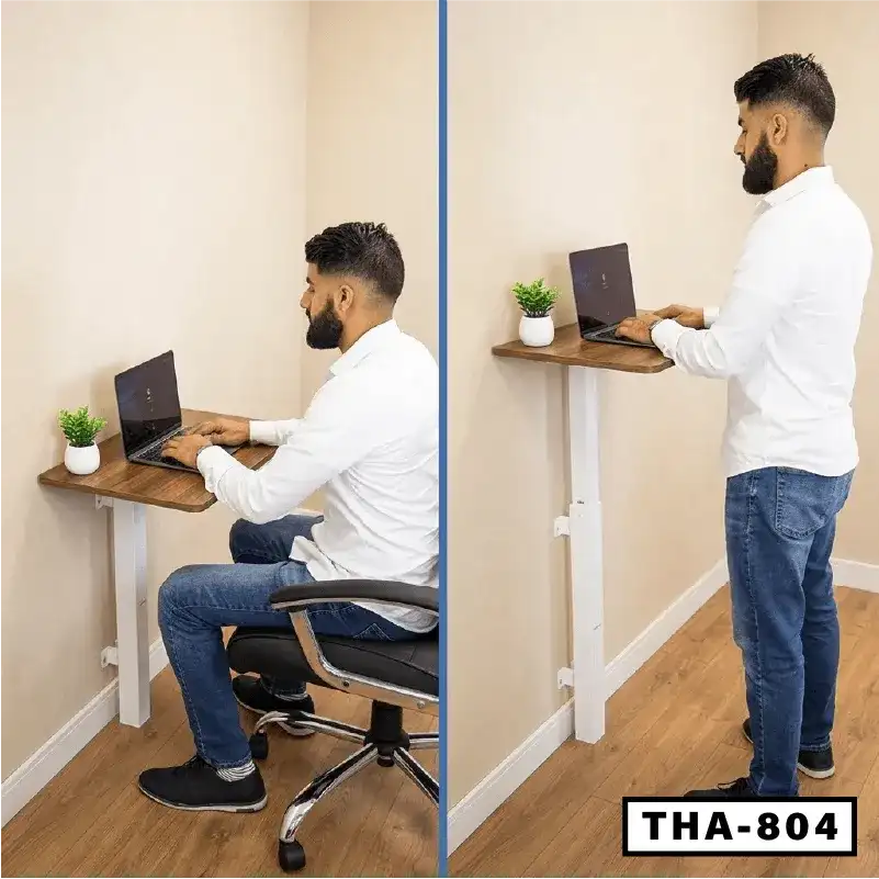 Adjustable wall-mounted laptop table used for sitting and standing, small potted plant on desk.