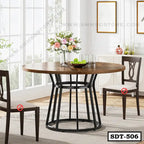 Modern round steel dining table with wood top, black metal base, surrounded by chairs in bright dining room