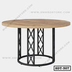 Round steel dining table with a wooden top and geometric black metal base on light background.