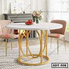 Modern round dining table with white top and gold steel base, flanked by two pink chairs in a stylish living room.