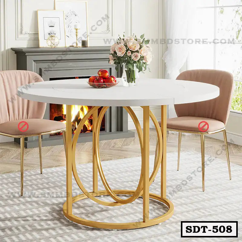 Modern round dining table with white top and gold steel base, flanked by two pink chairs in a stylish living room.