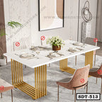 Modern steel dining table with white tabletop, gold legs, six upholstered chairs, and elegant table setting in a contemporary dining room.