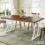 Modern steel dining table with wooden top in a bright dining room setting, chairs around, flowers and dishes on table.