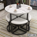 Modern steel dining table with round marble top and four white cushioned stools in a room setting.