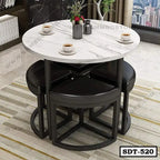 Modern round marble dining table with steel frame and four black cushioned stools in a living room.