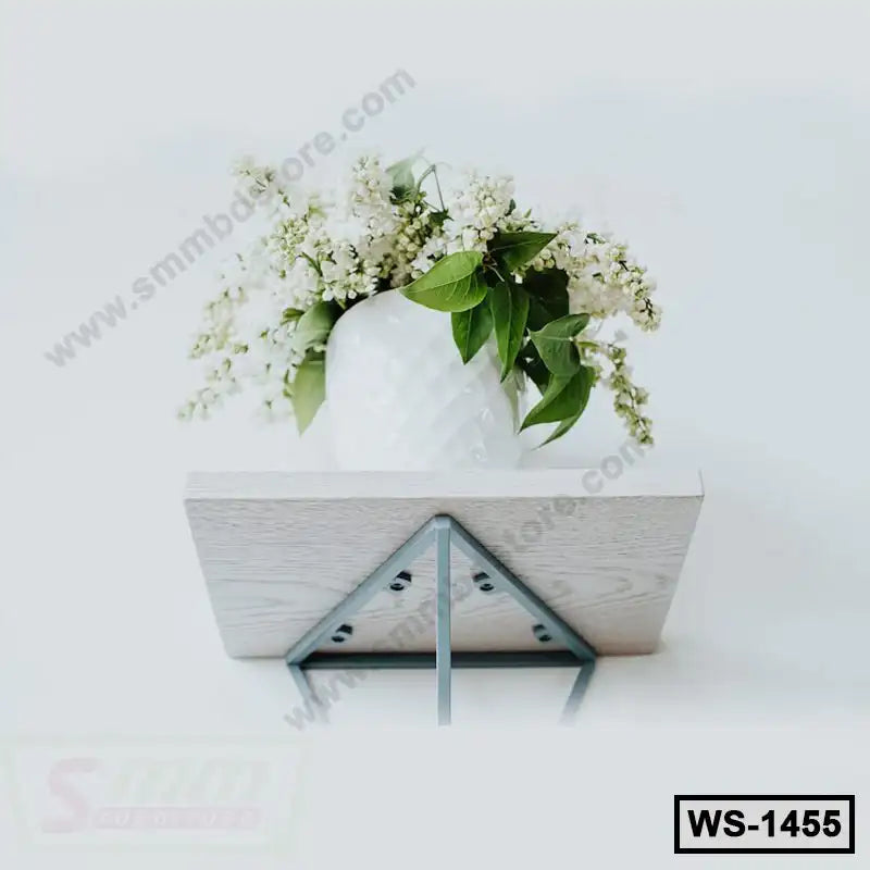 Minimalist wall shelf with metal brackets holding a white vase of blooming flowers