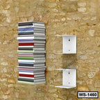 Modern wall-mounted white metal shelves holding stacked books on a rustic stone wall